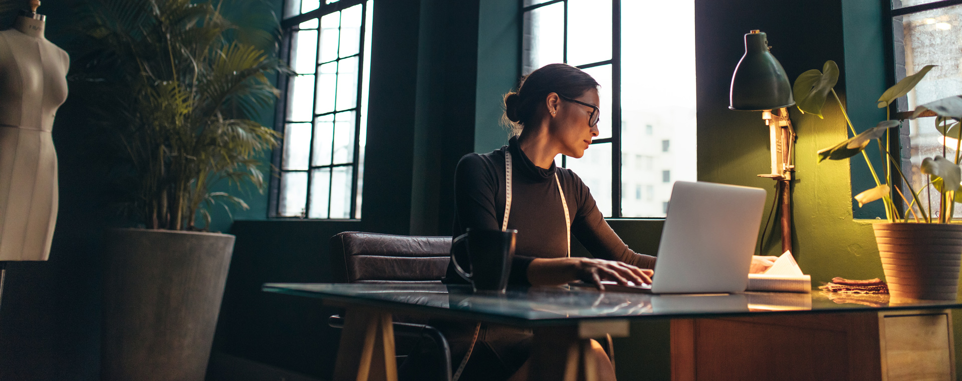 Fashion designer working at a desk with a laptop in a well-lit, stylish office.